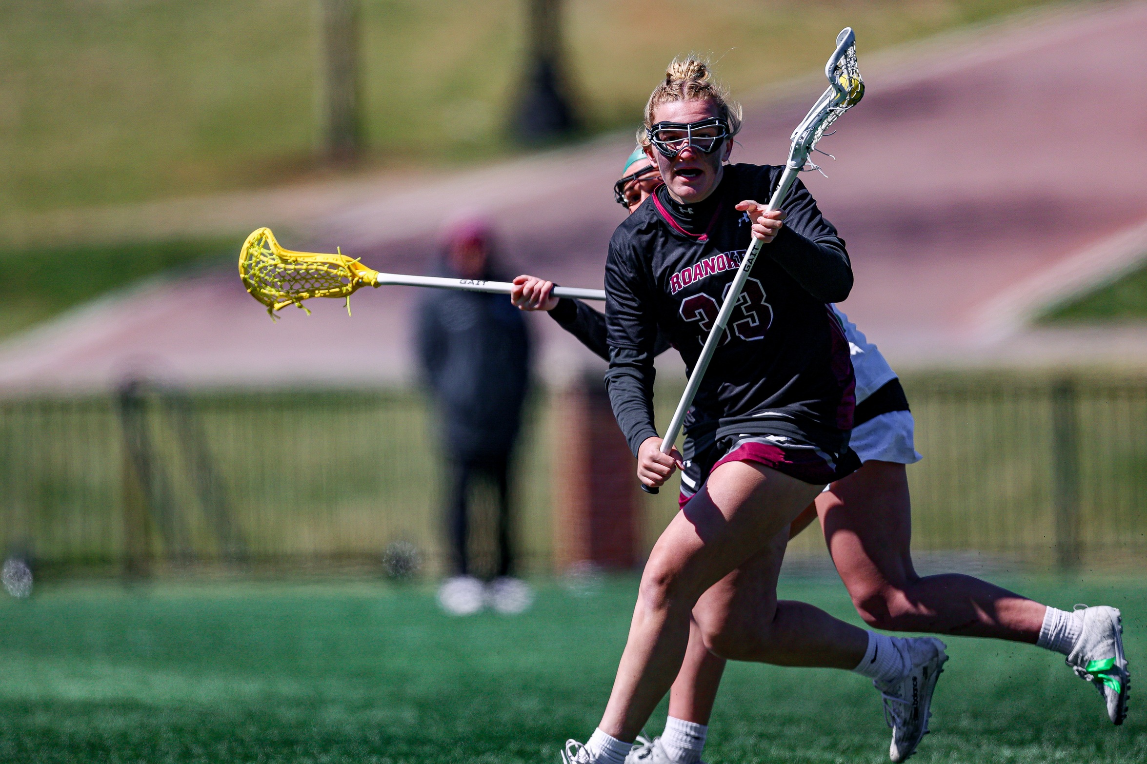 action photo of RC women's lacrosse player Grace Koutouzis with the ball and a defender on her back