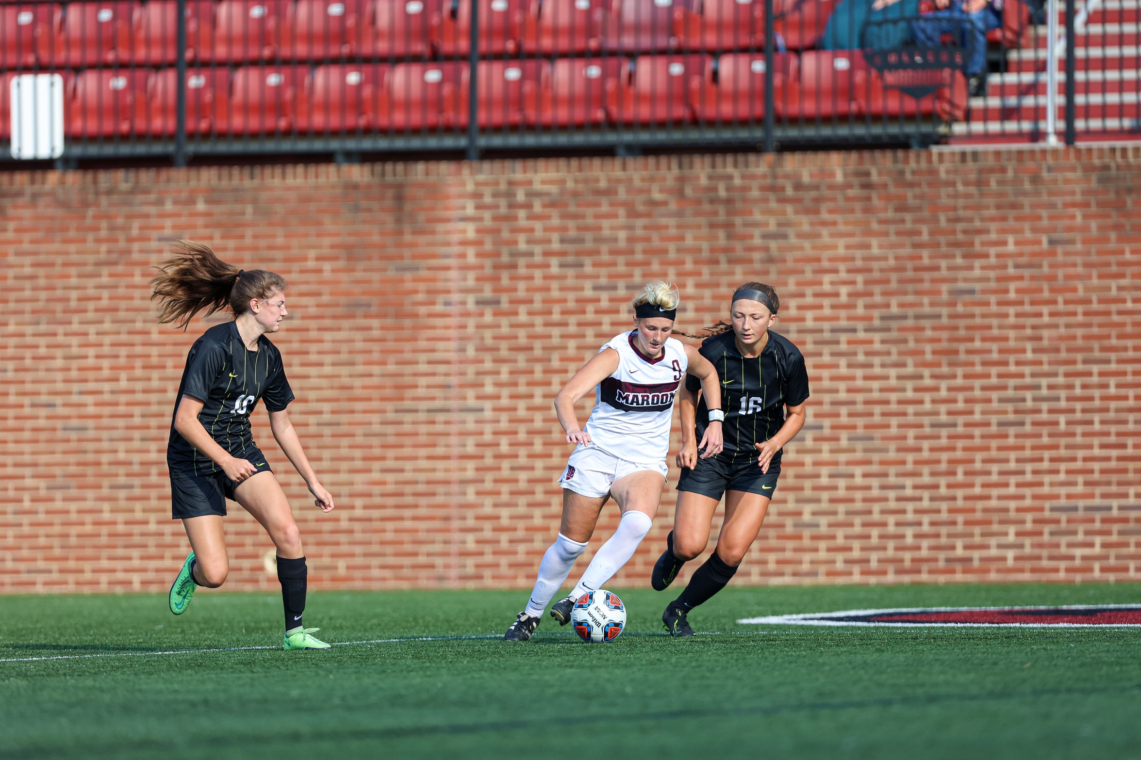 action photo of RC women's soccer player Cam Shackford (9) splitting a pair of defenders